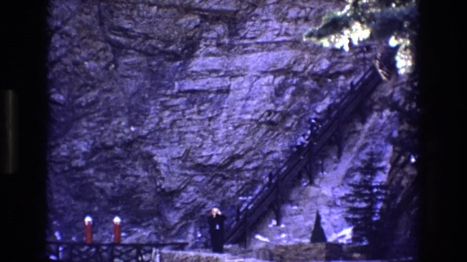 Final Colorado 1973 frame with a distant adult at the lower edge of a massive rock face and a narrow staircase climbing into shadow above them.