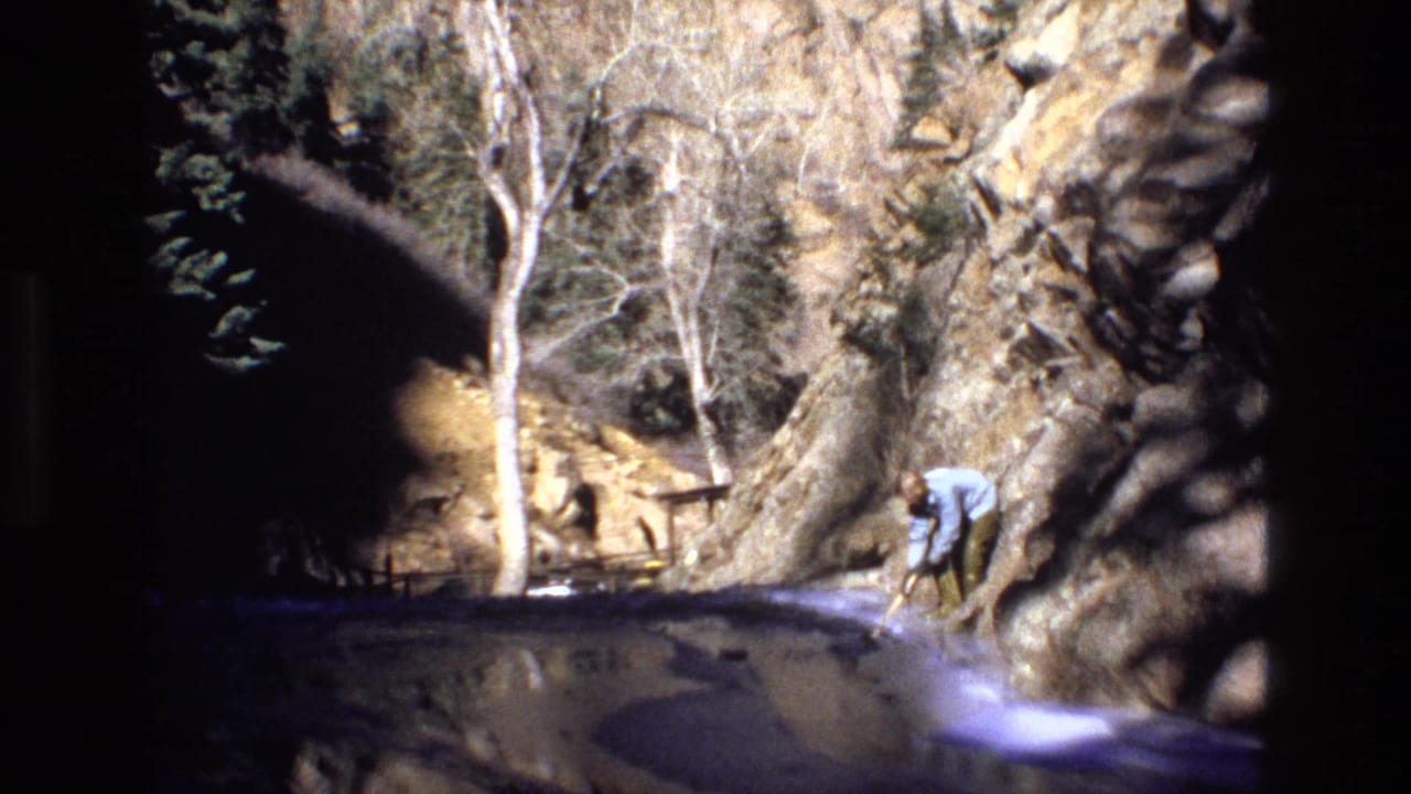 Rocky canyon beside water with bare trees and a man near the right edge.