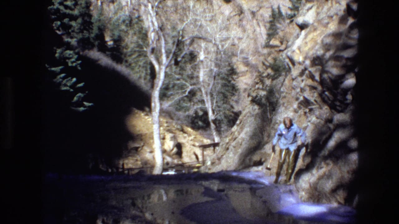 A hiker in a light blue shirt pauses near a shallow stream and rugged canyon rocks in metadata-supported 1973 Colorado footage.