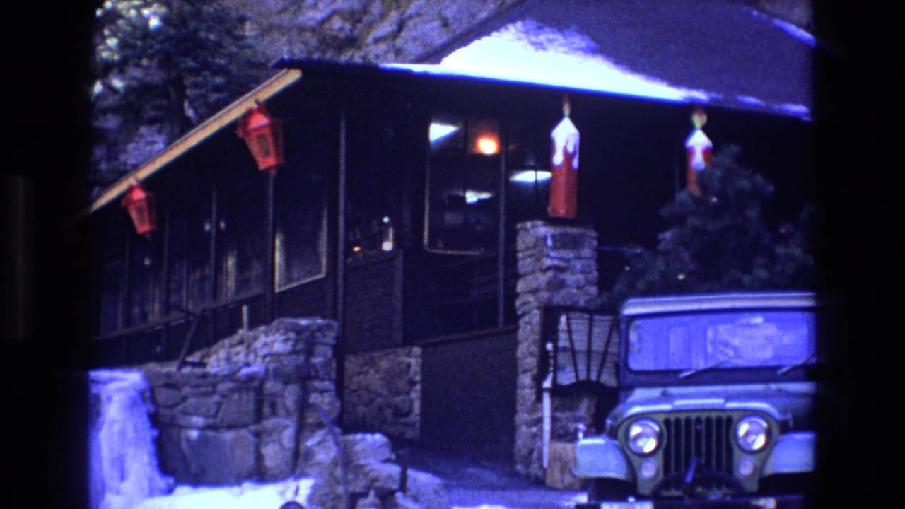 Snowy dark wood cabin with stone supports, red lanterns, and a parked Jeep-style vehicle.