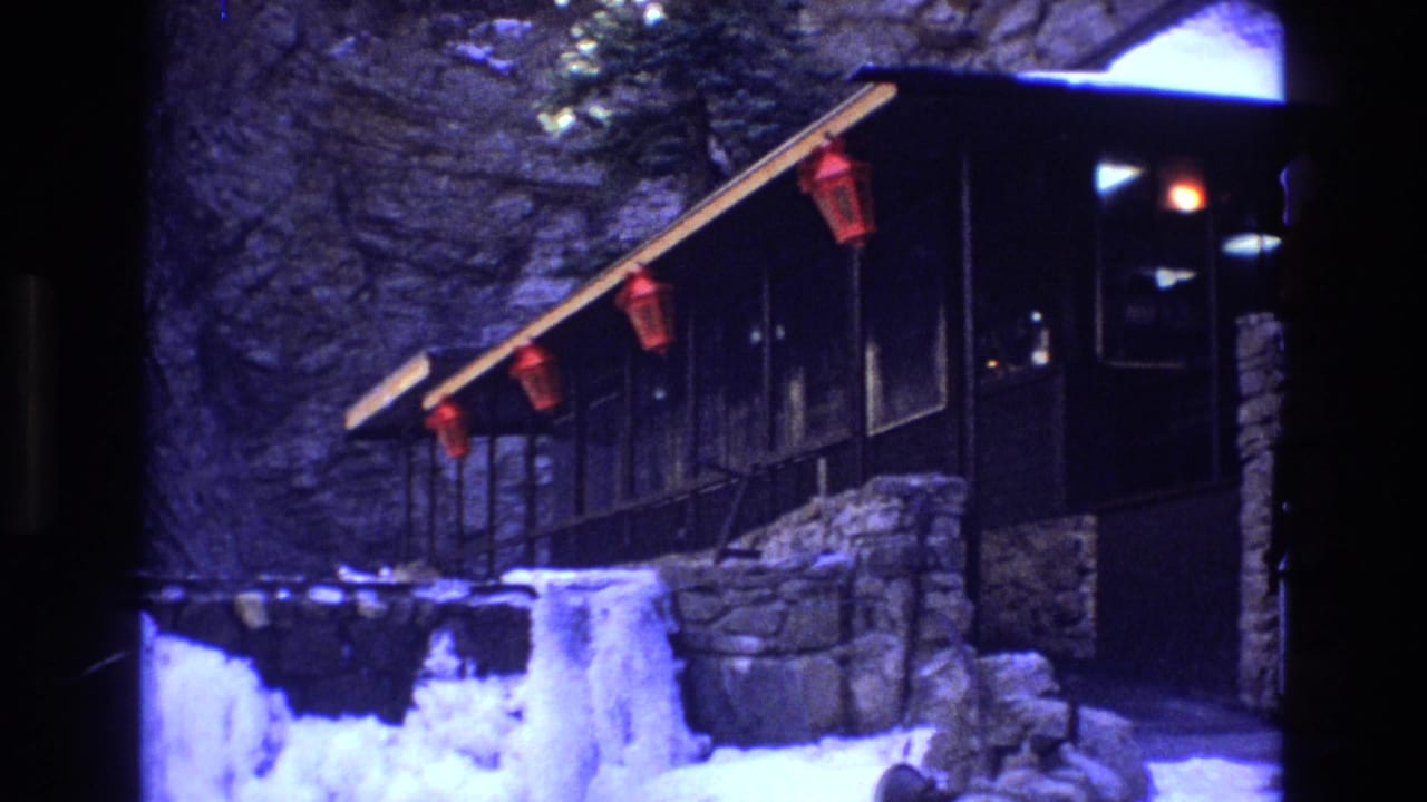 1973 Colorado 8mm frame showing a dark wooden mountain lodge porch with red lanterns, stonework, snowbanks, and ice in the foreground.