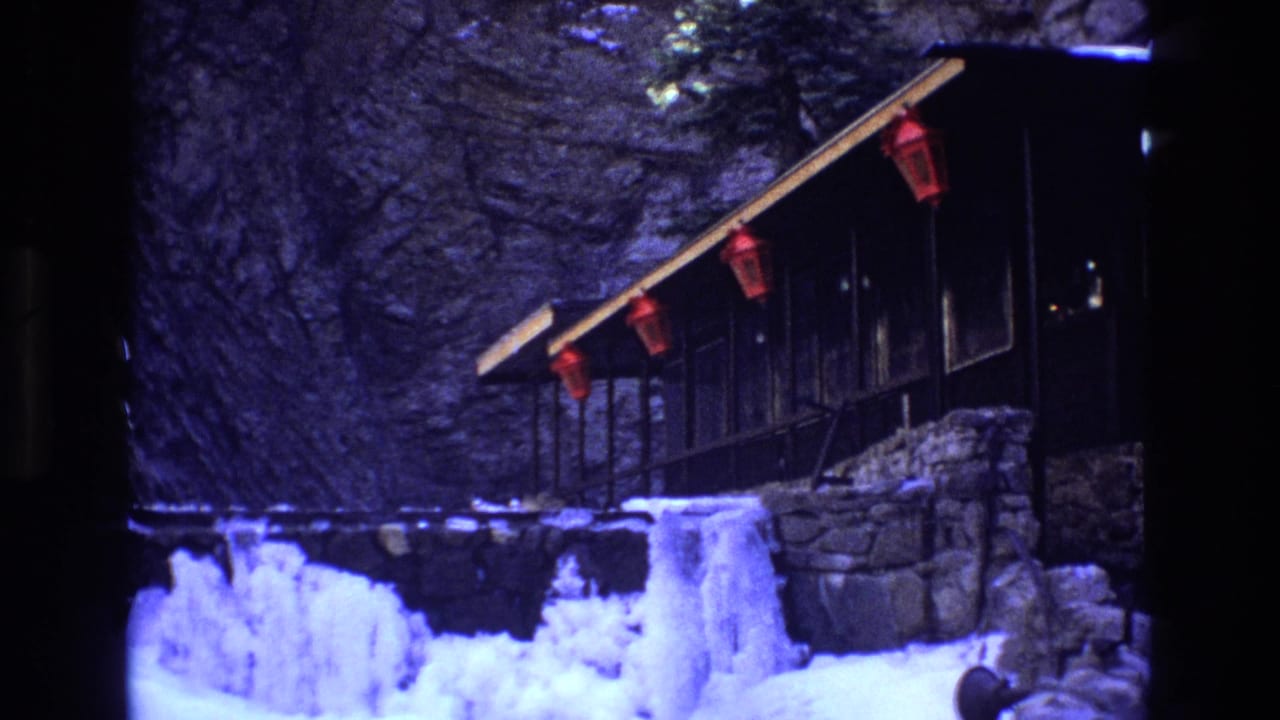 Snowy lodge exterior with lanterns and stone wall beside a cliff.