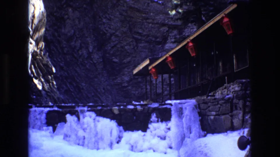 1973 Colorado 8mm frame with the camera shifted lower, showing heavy ice formations, a snowbank, stonework, and the lantern-lined porch above.