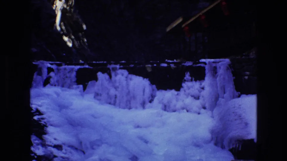 1973 Colorado 8mm frame with thick blue-purple ice formations, snow, a dark canyon wall, and red lights near the upper right edge.