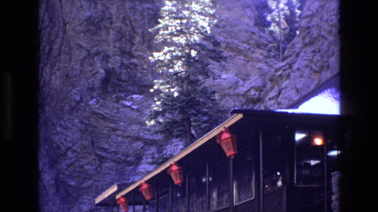 1973 Colorado 8mm frame showing a dark cabin exterior with red lanterns, snow, evergreen trees, and a sheer rock face behind it.