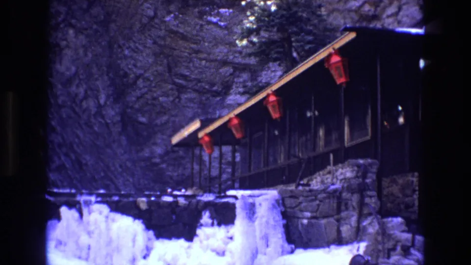 1973 Colorado 8mm frame showing a rustic cabin exterior, red lanterns, icicles, snow-covered ground, and rock behind the structure.