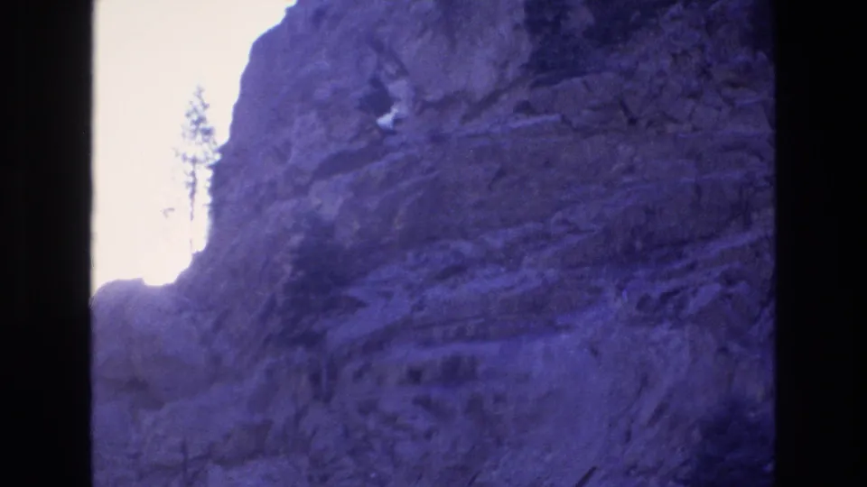 1973 Colorado 8mm frame looking between rugged mountain rock walls toward a bright opening, with a small evergreen tree silhouetted near the center.