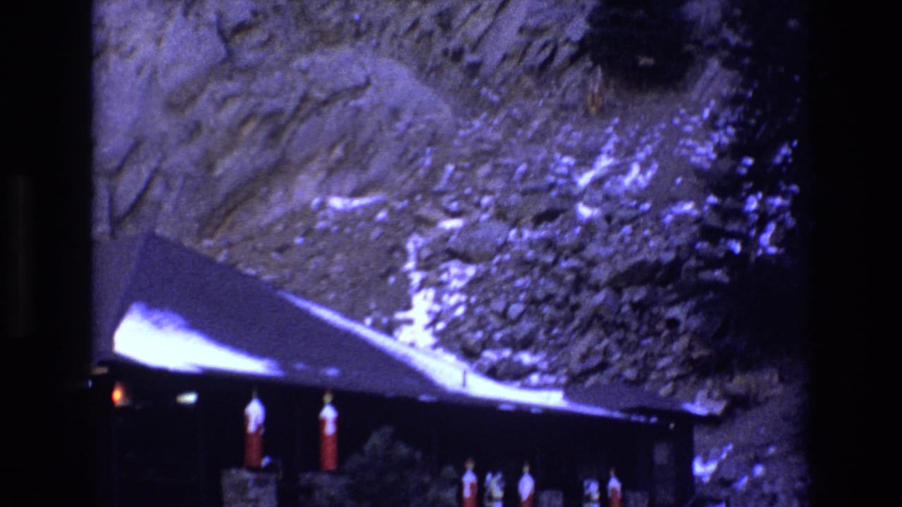1973 Colorado 8mm frame showing part of a dark rustic lodge below a rocky cliff, with snow on the roof and red lanterns under the eaves.