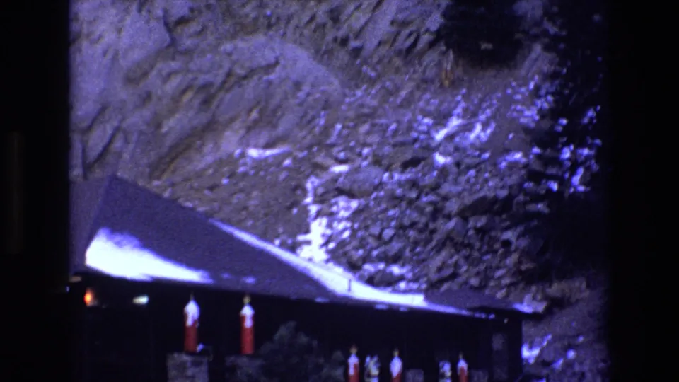 1973 Colorado 8mm frame showing part of a dark rustic lodge below a rocky cliff, with snow on the roof and red lanterns under the eaves.