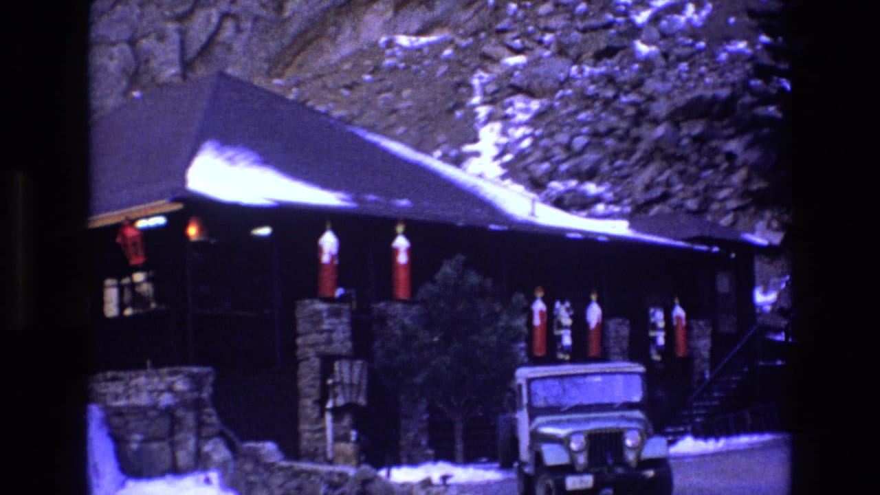 Rustic lodge below a cliff with red lanterns and a parked Jeep-like vehicle.