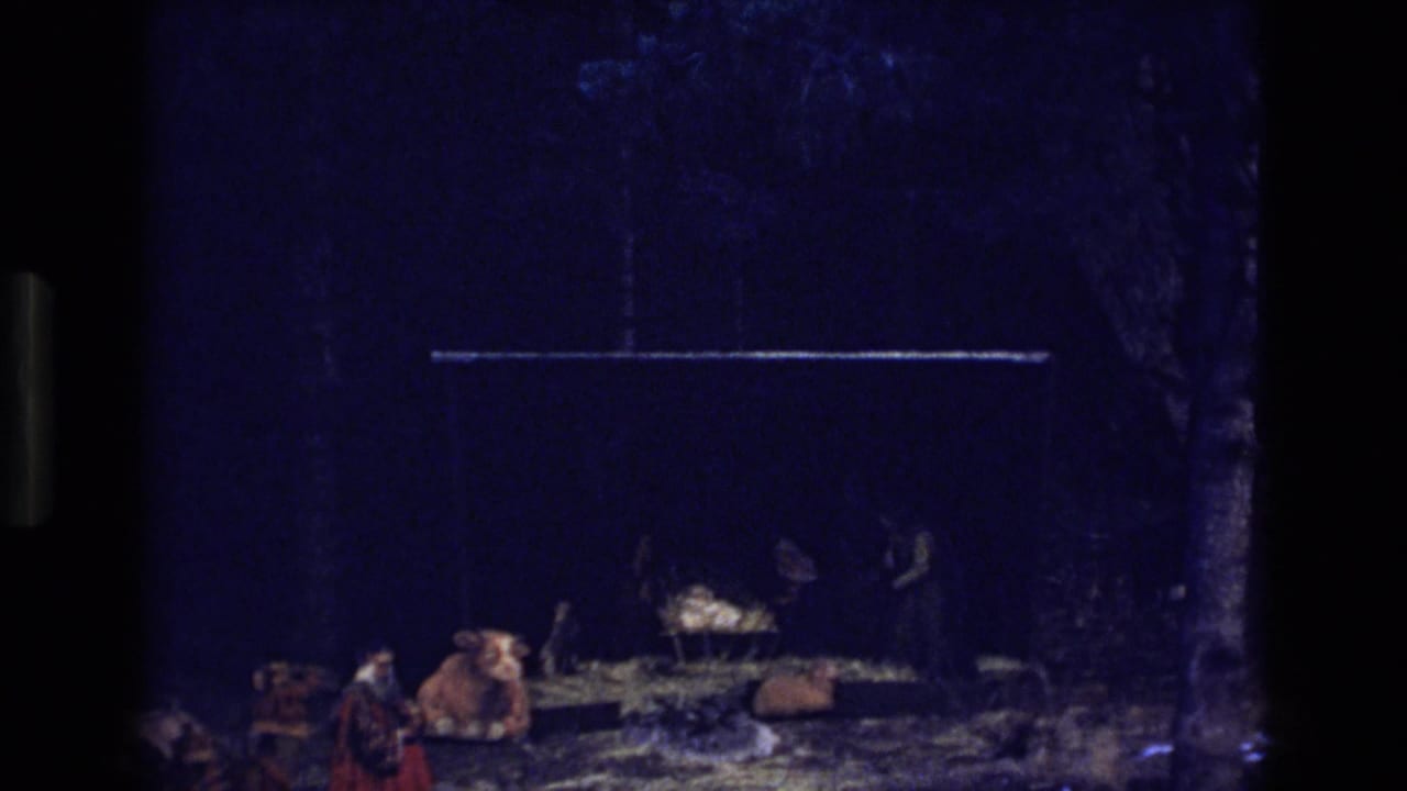 Nativity scene with cow, manger, hay, and dark figures near the cradle.