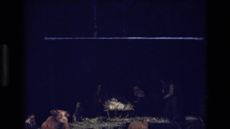 1973 Colorado 8mm frame showing a closer low-light view of the nativity tableau with a cow, straw-covered ground, cradle or manger, and several shadowed figures.