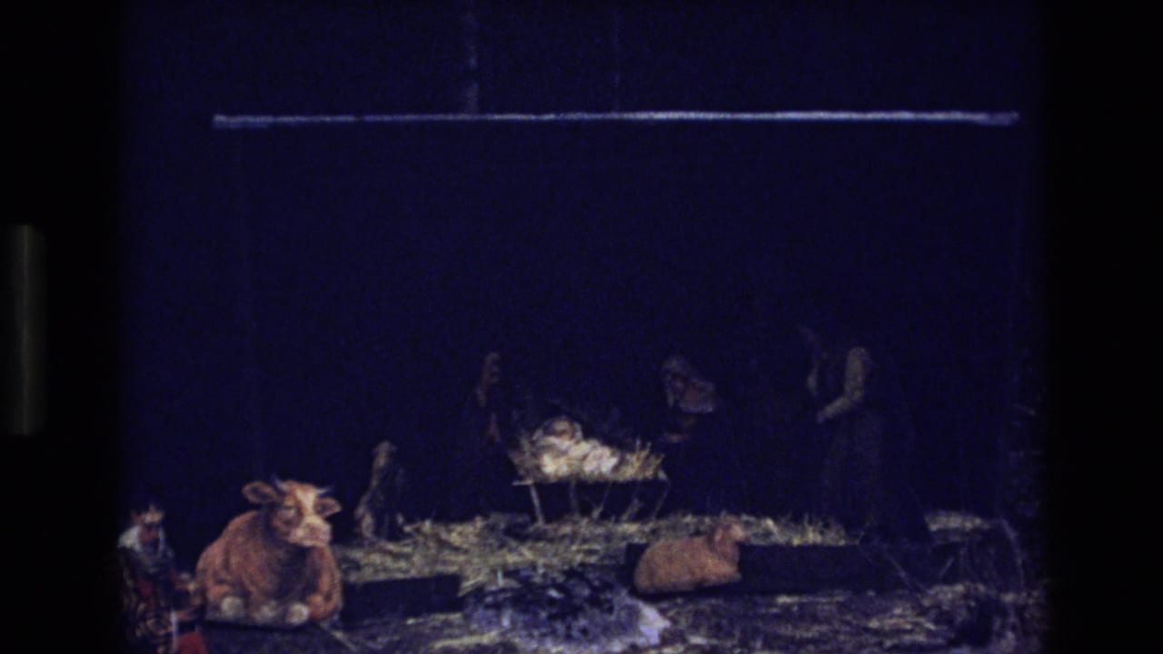 Dark 1973 Colorado 8mm frame showing a small nativity-style stable display with animal figurines and straw-like material in low light.