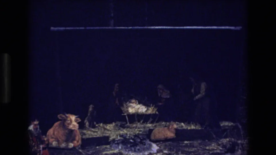 Dark 1973 Colorado 8mm frame showing a small nativity-style stable display with animal figurines and straw-like material in low light.