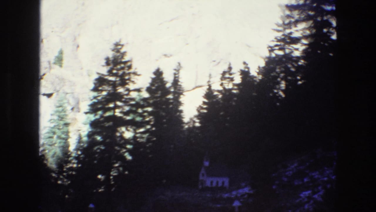 Evergreen trees silhouette against a sunlit rock face with a small chapel at lower right.