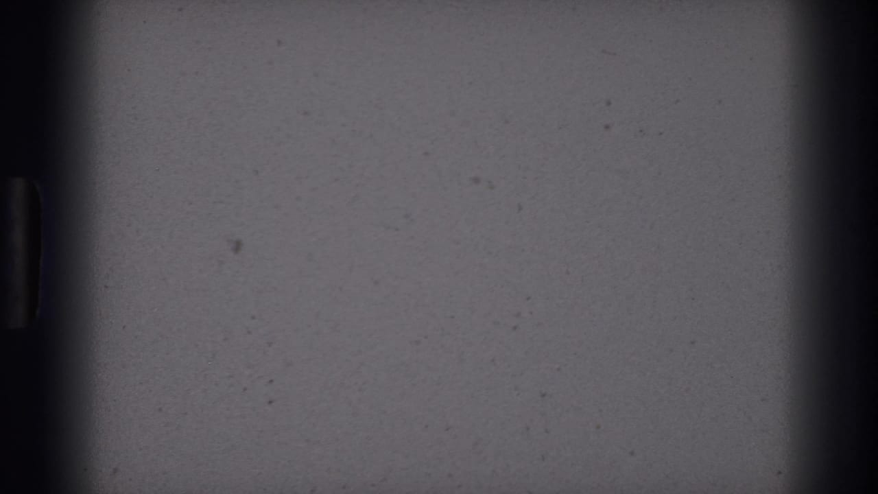 Mostly blank 8mm frame area with dark vertical gate edges and small film specks before the Colorado Springs rodeo sign appears.