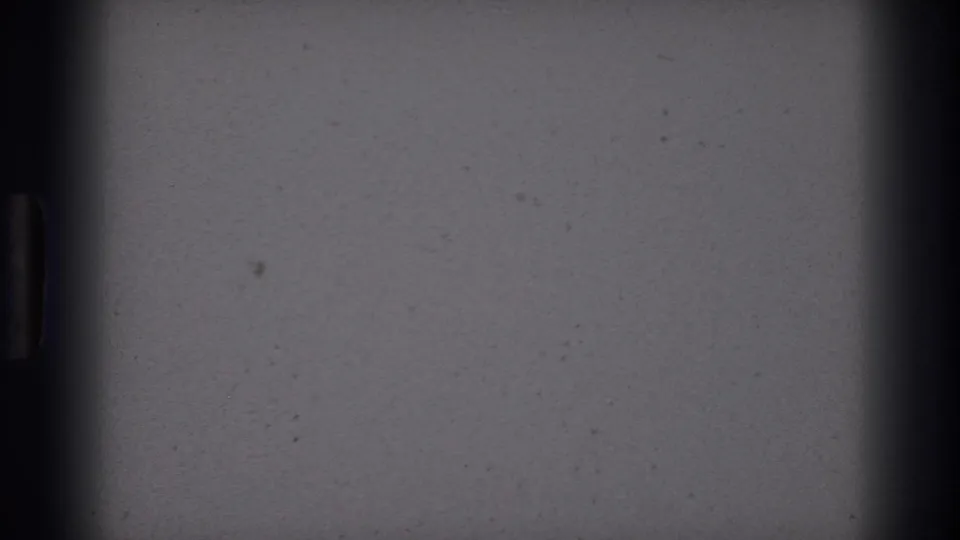 Mostly blank 8mm frame area with dark vertical gate edges and small film specks before the Colorado Springs rodeo sign appears.