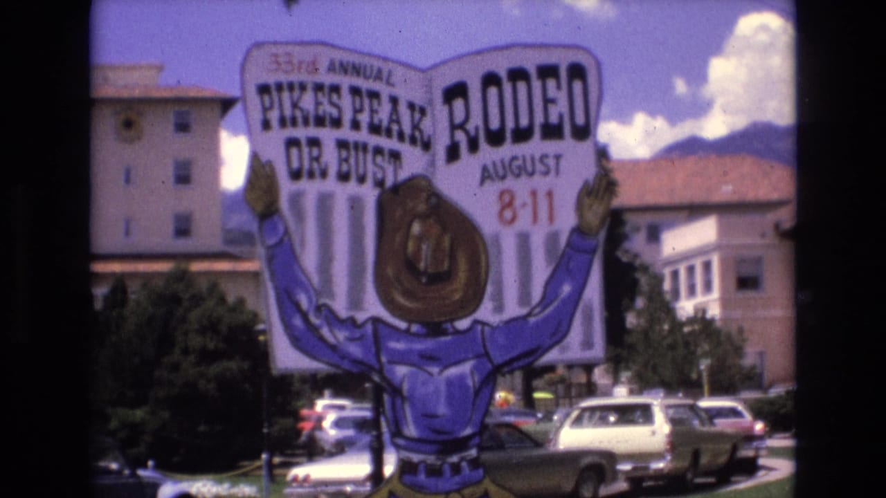 1973 Colorado Springs 8mm frame showing a colorful cowboy-shaped sign for the 33rd Annual Pikes Peak Rodeo, August 8-11, with parked cars, trees, and buildings in the background.