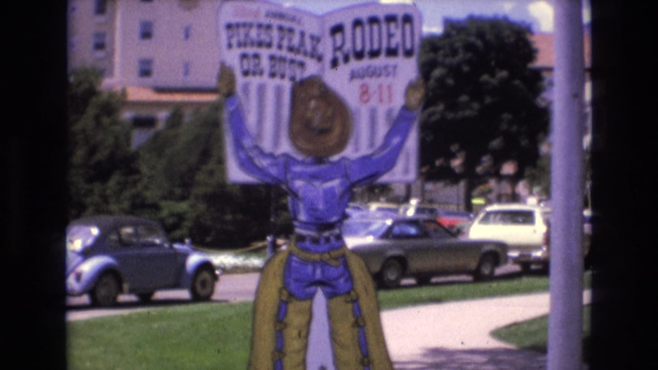 Rodeo sign held by a cowboy figure beside parked cars and a sidewalk.