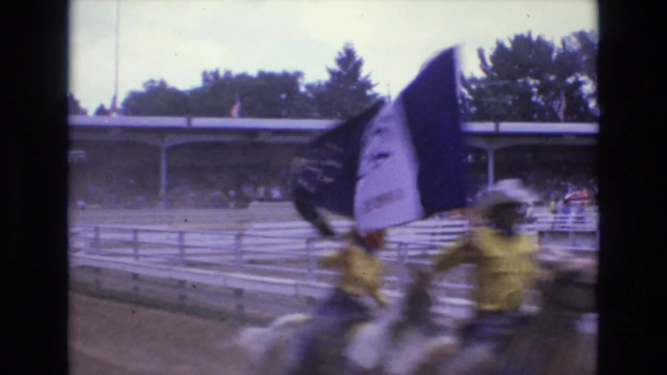 A large flag partially obscures mounted riders in yellow shirts during a 1973 rodeo flag procession in Colorado Springs.