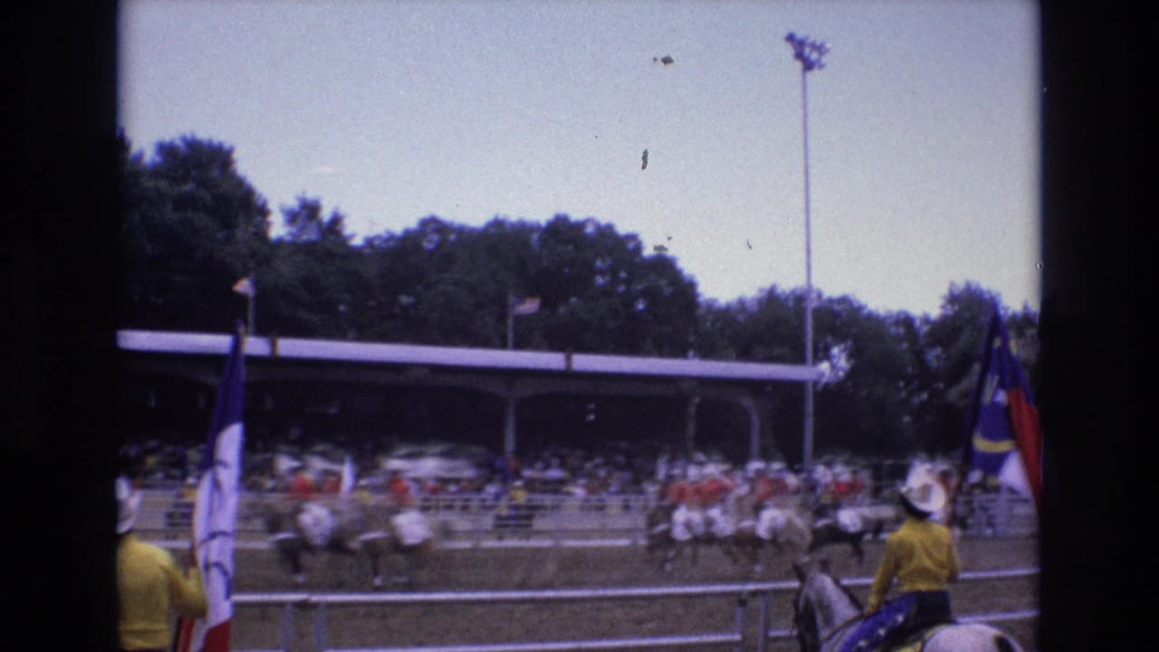 Mounted riders in red and white clothing move across the arena in front of spectators.
