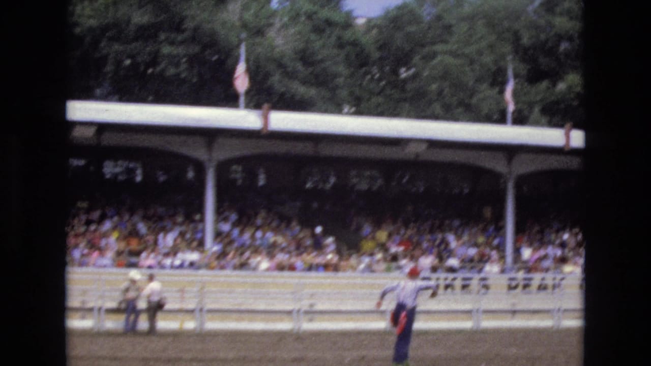 Crowd in covered arena seating with people standing near the rail.