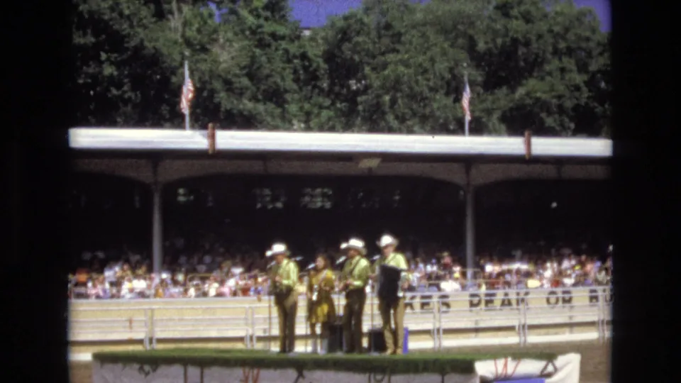 A 1973 Colorado Springs outdoor performance shows male musicians in white cowboy hats beside a female vocalist, with spectators filling the pavilion behind them.