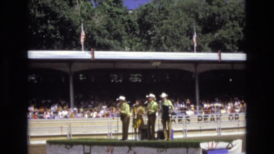 The home-movie view captures a brief movement during the Colorado Springs country performance, with the band grouped on a small stage and the pavilion audience behind them.