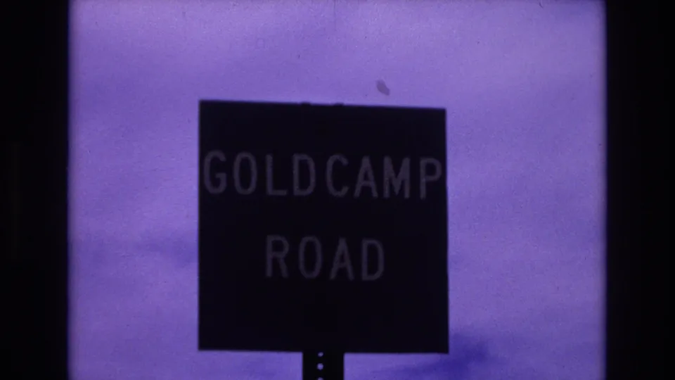 Colorado Springs home-movie frame showing a dark roadside sign reading Gold Camp Road against a purple-tinted sky and soft 8mm exposure.
