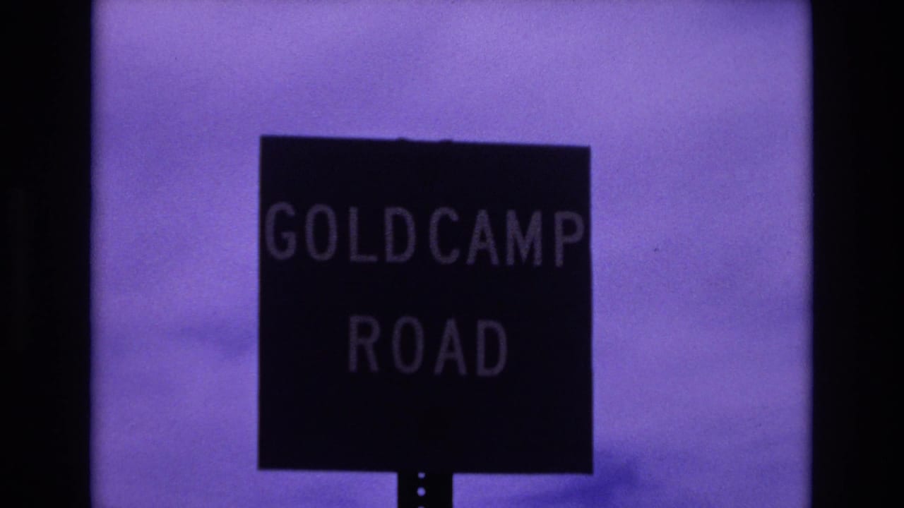 1973 Colorado Springs home-movie frame showing a black Goldcamp Road sign with pale lettering against a purple-tinted sky.