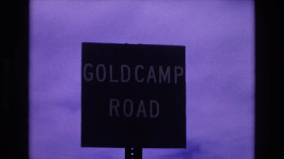 1973 Colorado Springs home-movie frame showing a black Goldcamp Road sign with pale lettering against a purple-tinted sky.
