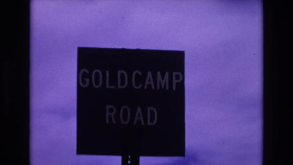 Final 1973 Colorado Springs frame holding on the dark Goldcamp Road sign beneath a purple-tinted sky and soft horizon line.