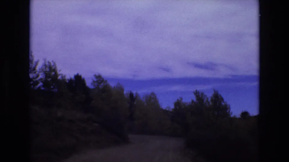 1973 Colorado Springs home-movie frame showing a winding dirt road through wooded hills under a cloudy blue-purple sky.