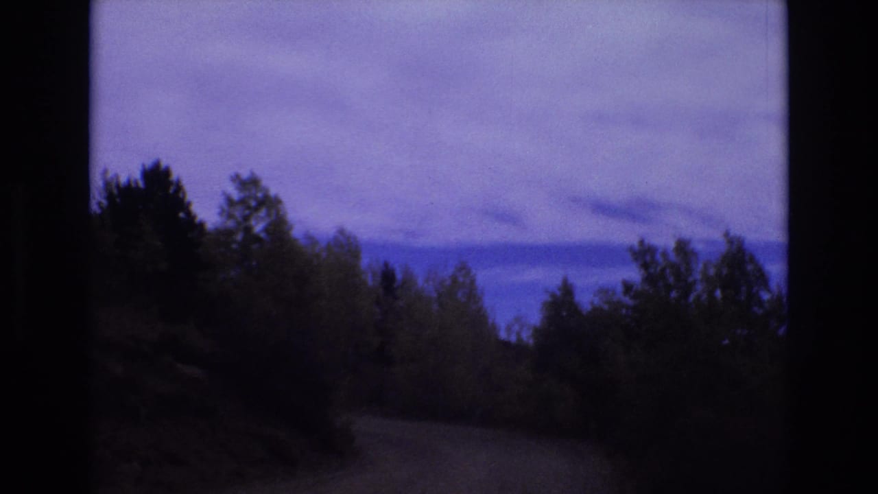 Curving rural road passing between trees and low hills.