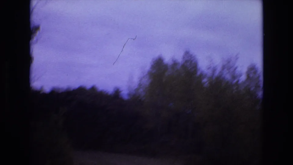 1973 8mm home-movie frame from the Colorado Springs clip showing a dark mountain roadside with brush, distant tree line, and a purple-blue sky framed by black gate edges.