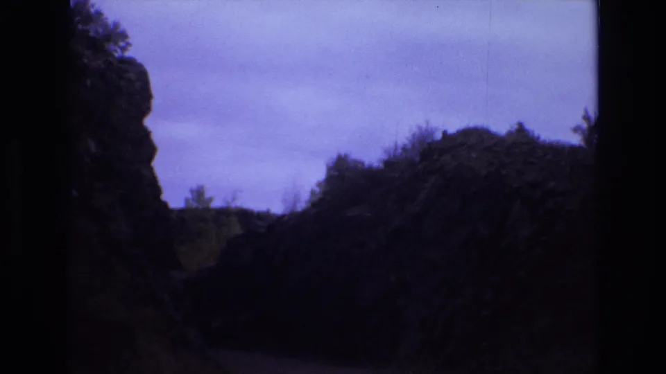 1973 8mm travel frame from Colorado Springs showing close dark rock walls, scrub vegetation, and open sky from a moving visitor-shot perspective.