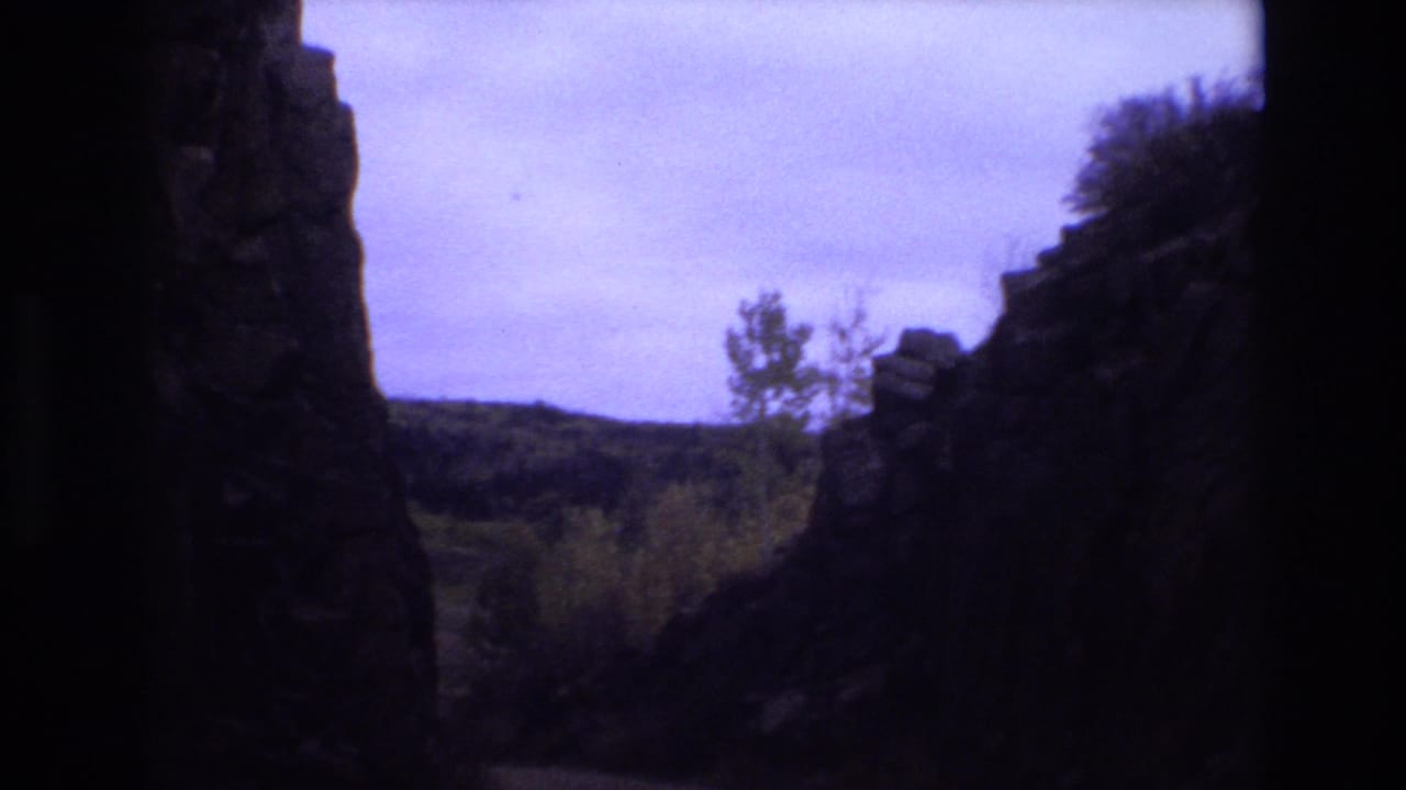1973 Colorado Springs 8mm frame showing shadowed rock formations around a narrow view of wooded hills and a cloudy purple-tinged sky.