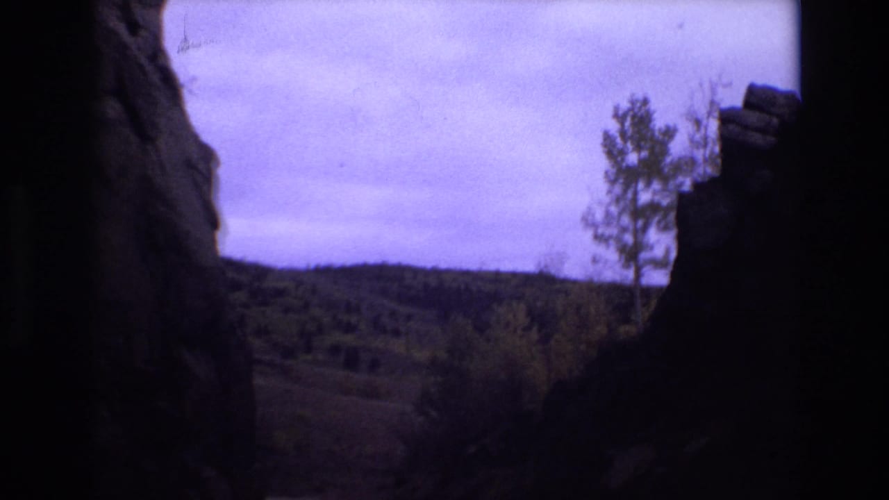 A central dark rock column divides views of hills, trees, and sky.
