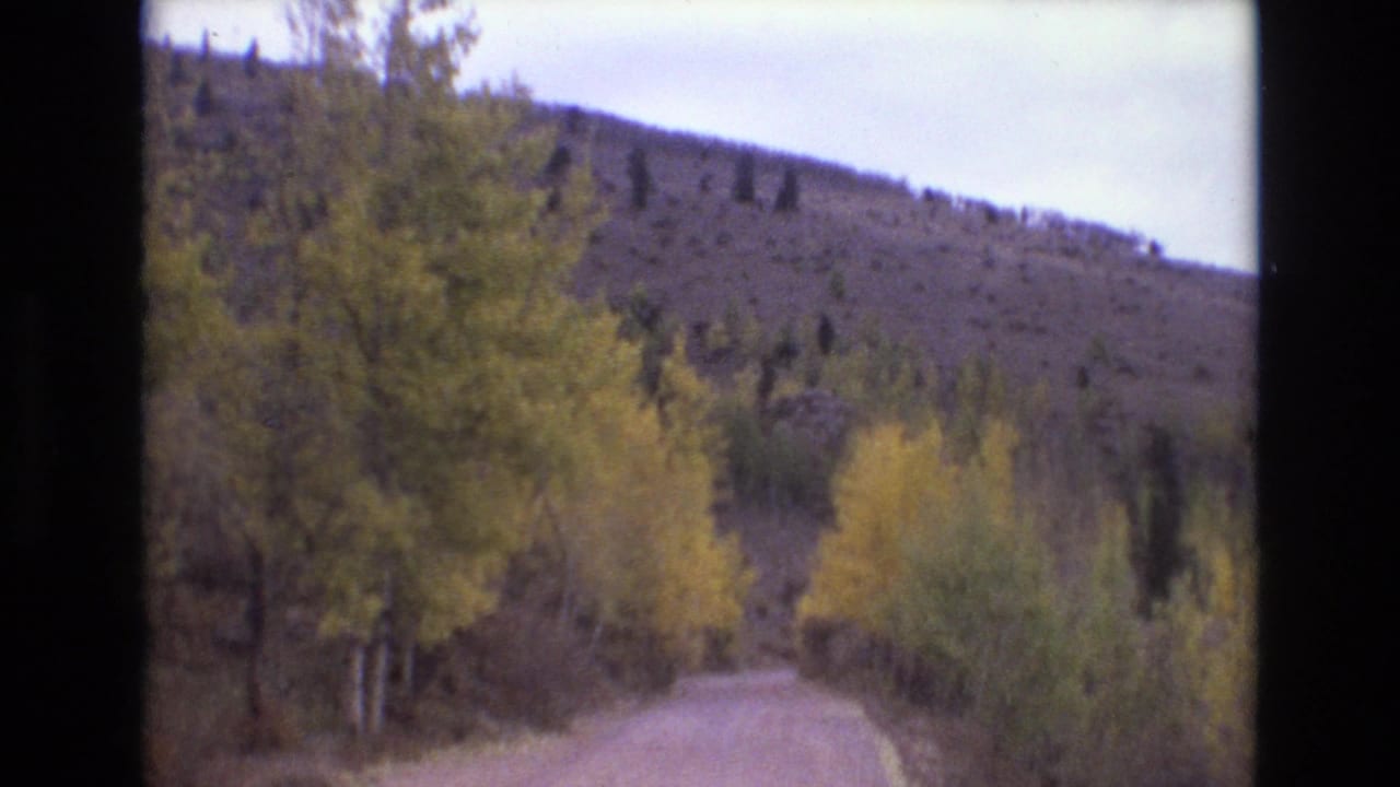 1973 Colorado Springs-area 8mm frame showing a dirt mountain road bordered by yellow-green autumn trees and a rocky hillside.