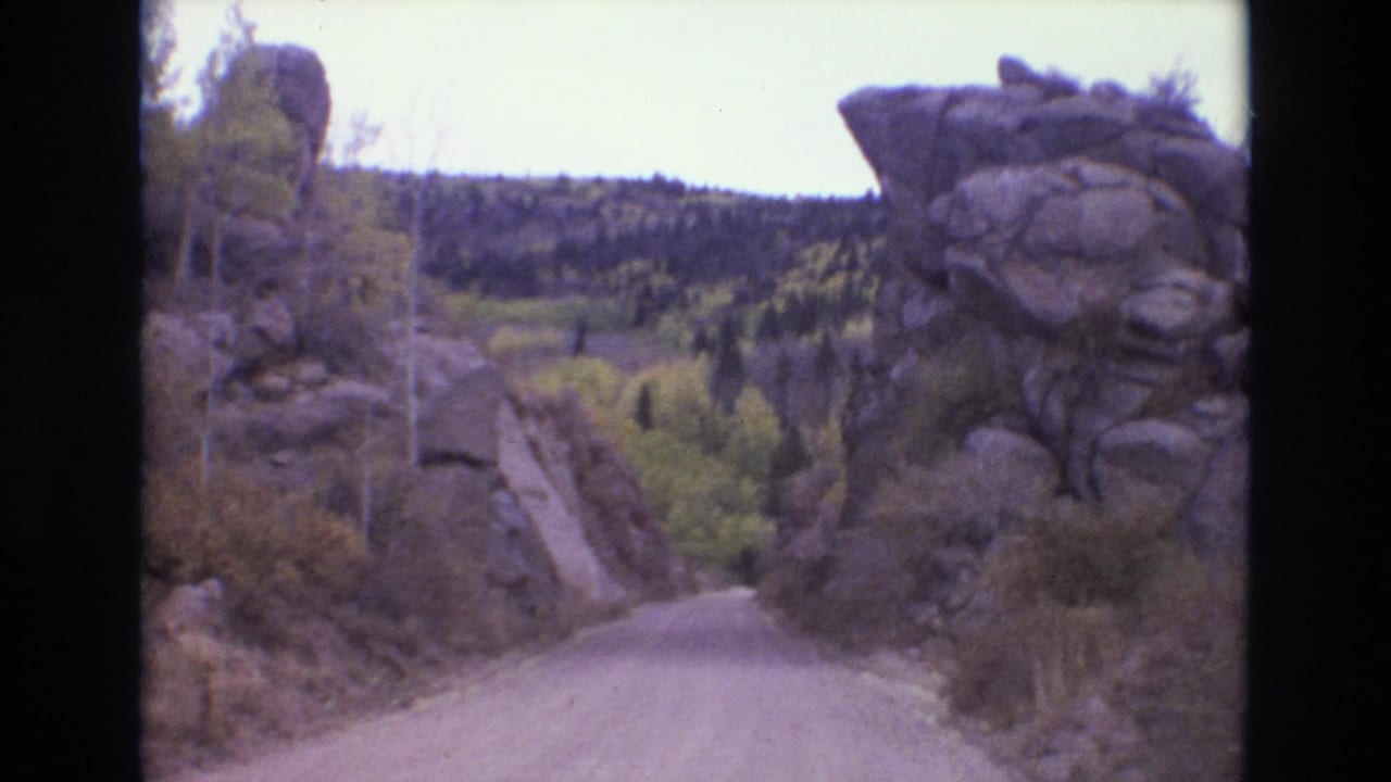 Unpaved road curving between tall rock formations and trees.
