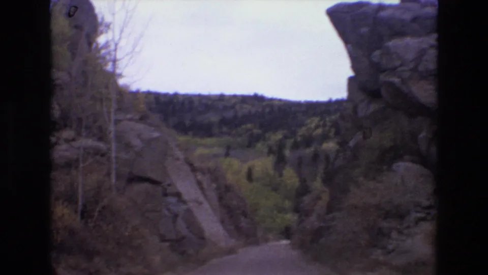 8mm home-movie frame from the Colorado Springs-area road trip, showing a dirt road squeezed between large rock faces and wooded hills.