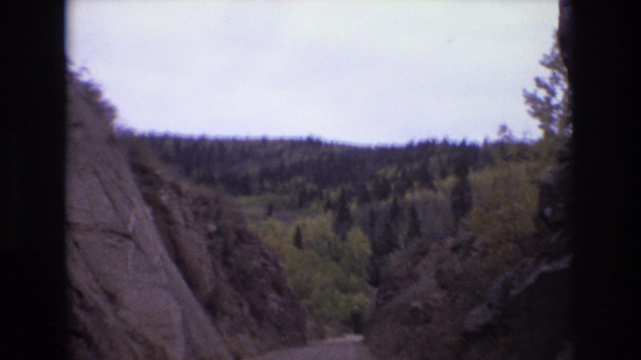 Forward view between rock walls toward a tree-covered hillside.