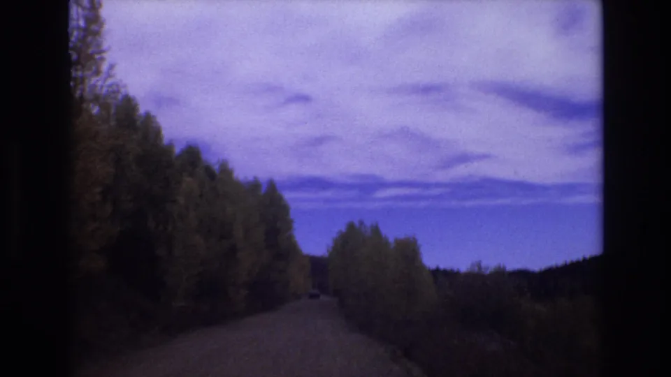 Final 1973 Colorado Springs frame showing the road continuing between dark forested slopes beneath a purple-blue evening sky with visible film color shift.