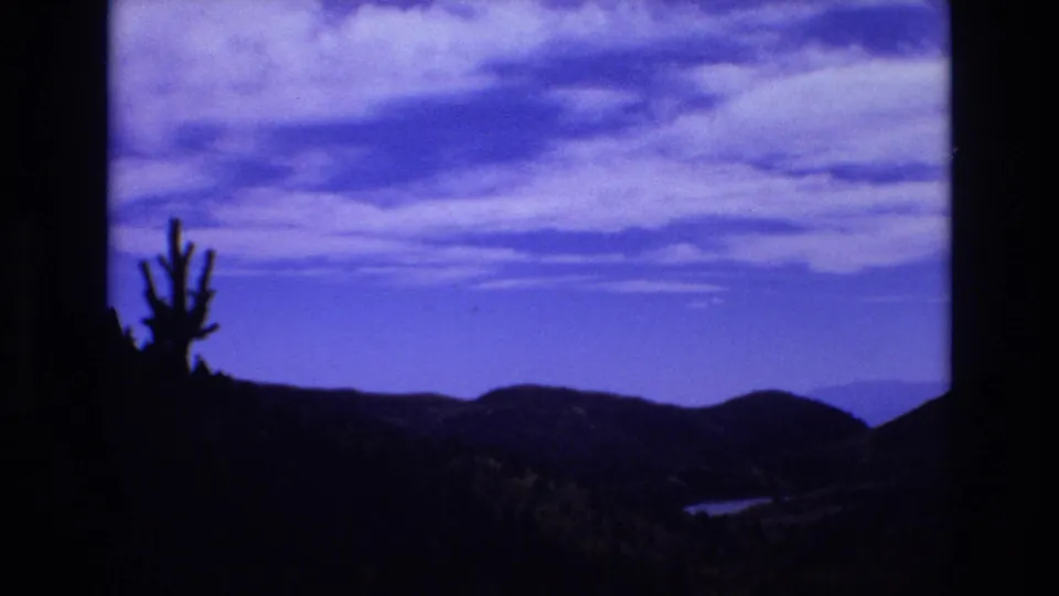 1973 Colorado Springs travel frame with a cactus-like plant silhouette, dark mountain ridges, and a blue sky with layered clouds.