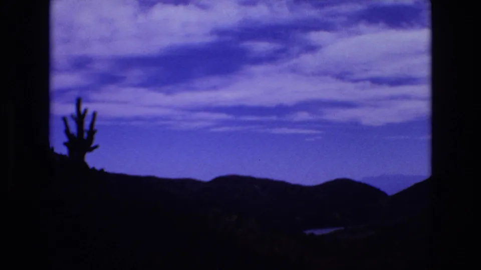 1973 Colorado Springs 8mm frame showing a dark ridgeline, a cactus-like silhouette, and a broad blue-and-white sky from a scenic travel viewpoint.
