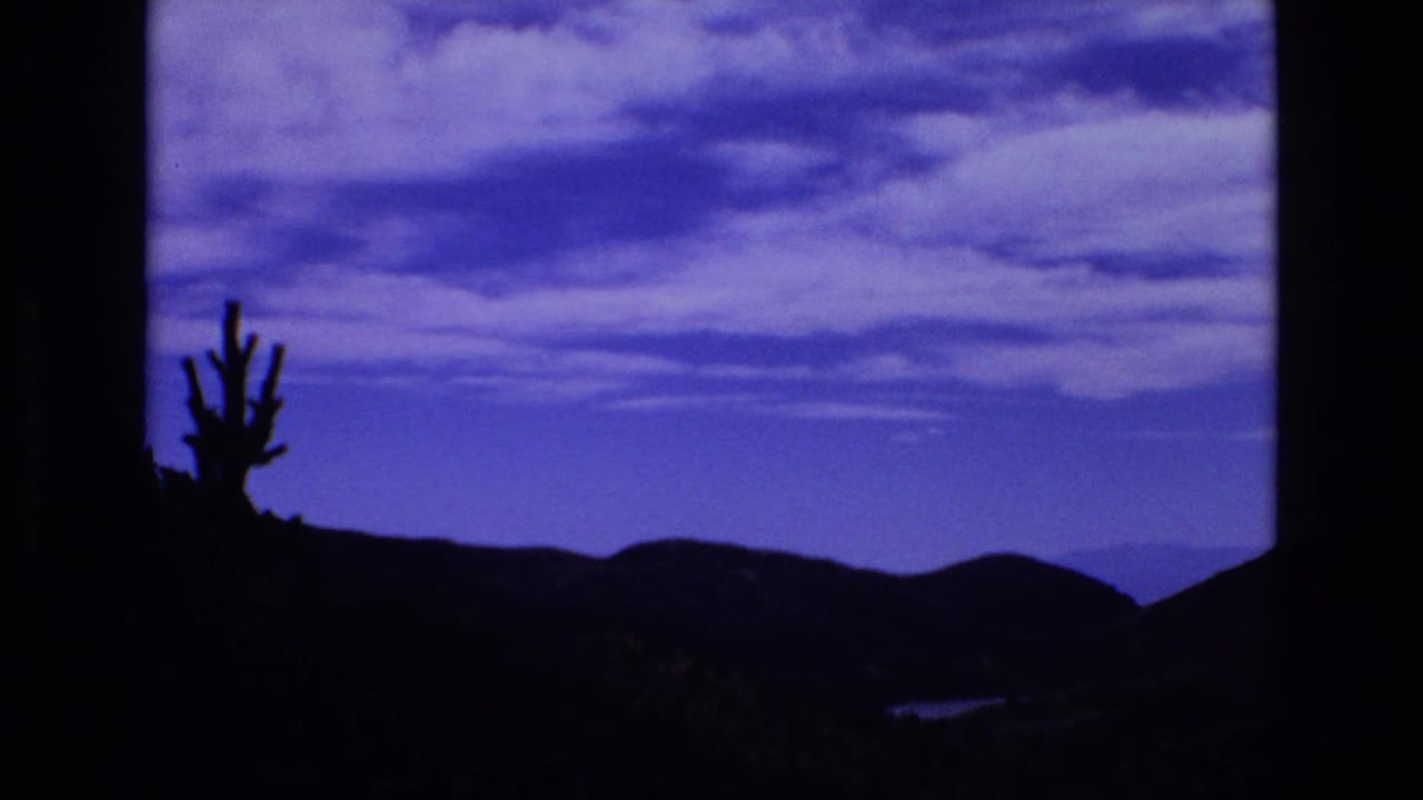 1973 8mm home-movie frame from the Colorado Springs metadata showing a cactus-like silhouette, dark rolling hills, and a blue-purple clouded sky at dusk or night.