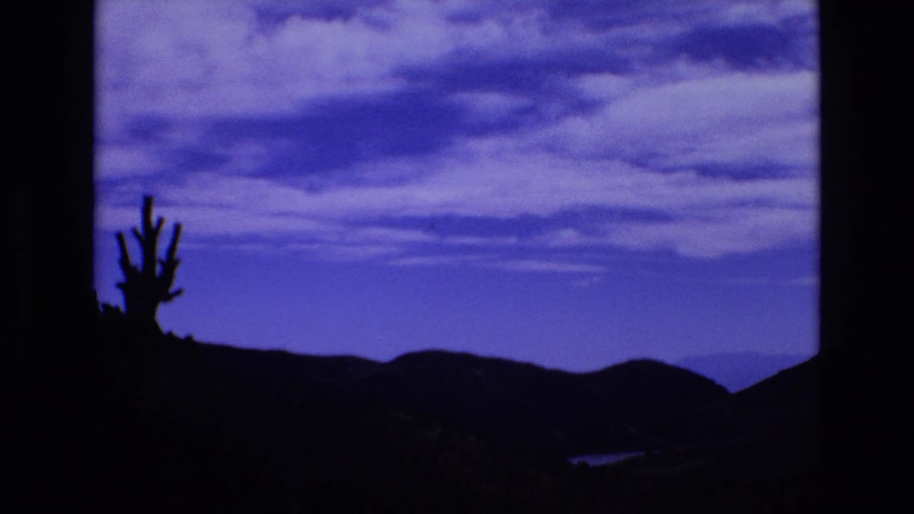 Static 8mm frame with a cactus-like plant in silhouette, distant hills, and a saturated blue evening sky consistent with the Colorado Springs 1973 clip metadata.