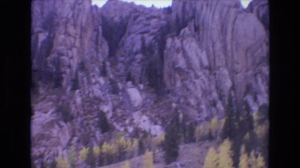 1973 Colorado Springs 8mm frame showing rugged vertical rock formations with conifers and a pale path or wash near the base.
