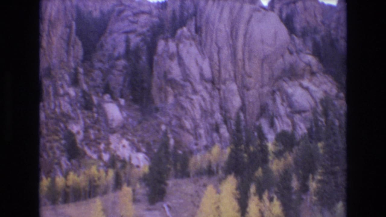 1973 8mm home-movie frame from Colorado Springs showing pale rugged rock formations rising above pines and autumn-colored trees.