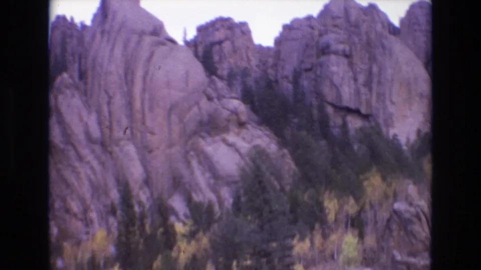 1973 Colorado Springs 8mm frame showing a rocky cliff wall and pointed formation with evergreen pines and yellow autumn foliage in the foreground.